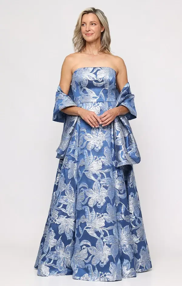 A woman wearing a strapless blue and silver floral gown with an off-the-shoulder cape.